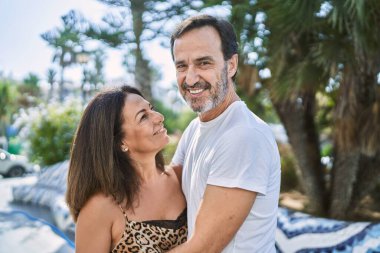 Orta yaşlı erkek ve kadın çift gülümsüyor. Kendilerine güveniyorlar. Sokakta birbirlerine sarılıyorlar.