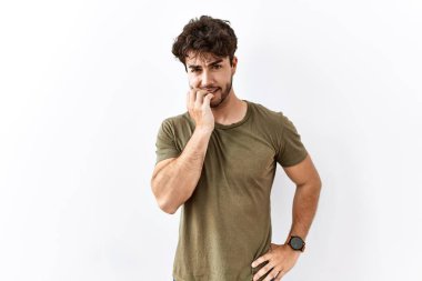 Hispanic man standing over isolated white background looking stressed and nervous with hands on mouth biting nails. anxiety problem. 