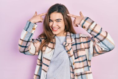 Gündelik giysiler giymiş genç beyaz bir kız iki eliyle başını gösteren gülümseme, harika bir fikir ya da düşünce, iyi bir hafıza. 