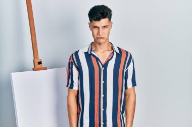 Genç İspanyol bir adam boş tuvalin yanında depresif ve endişeli bir şekilde duruyor. Kızgın ve korkmuş bir şekilde ağlıyor. hüzünlü ifade. 