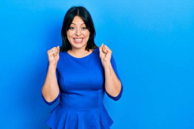 Gündelik giysiler giyen genç İspanyol kadın şaşkınlık ve şaşkınlık içinde kollarını kaldırarak ve gözlerini açarak başarıyı kutluyor. Kazanan konsept. 