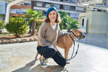 Genç beyaz kadın gülümsüyor. Parkta kendine güvenen bir köpek.