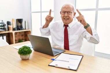 Ofiste çalışan kıdemli adam bilgisayarını kullanıyor. Şaşırmış ve şaşırmış bir şekilde gülümsüyor ve parmaklarıyla işaret ediyor.. 
