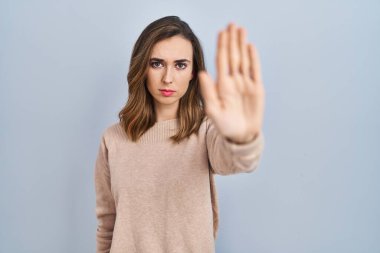 Young woman standing over isolated background doing stop sing with palm of the hand. warning expression with negative and serious gesture on the face. 