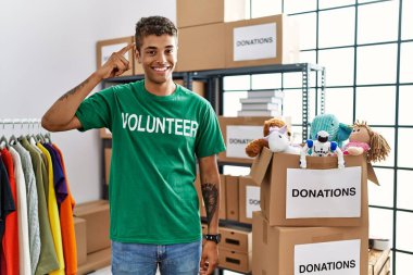 Bağışlarda gönüllü tişört giyen yakışıklı İspanyol genç adam gülümseyerek tek parmağıyla, harika bir fikirle ya da düşünceyle, iyi bir hafızayla ayakta duruyor. 