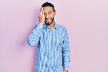 Sakallı, sıradan mavi tişörtlü, bir gözünü eliyle kapatan İspanyol bir adam, yüzünde kendine güvenen bir gülümseme ve sürpriz bir duygu.. 