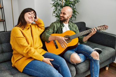 Genç İspanyol çift gülümseyerek evde kanepede oturmuş klasik gitar çalıyor..