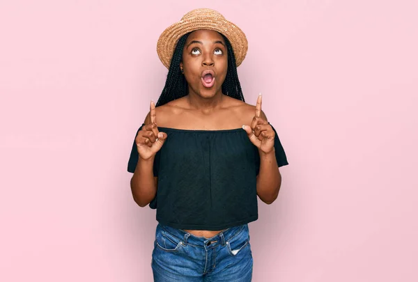 夏の帽子をかぶっている若いアフリカ系アメリカ人の女性は驚きと驚きを見上げ 指で指して腕を上げた — ストック写真