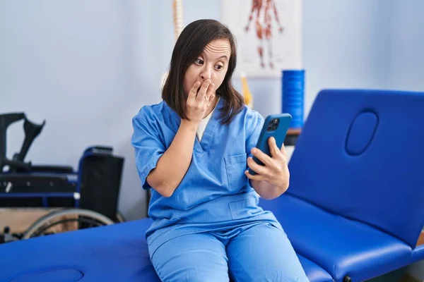 Латиноамериканка Синдромом Дауна Работающая Физиотерапии Используя Смартфон Прикрывающий Рот Рукой — стоковое фото