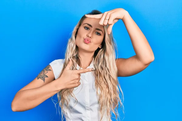 Beautiful young blonde woman doing picture frame gesture with hands looking at the camera blowing a kiss being lovely and sexy. love expression.