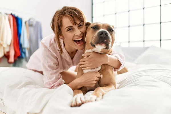 Young caucasian woman hugging dog lying on bed at bedroom