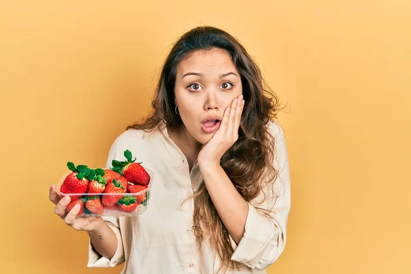 年轻的慌张女孩拿着草莓 脸上带着恐惧 惊奇和惊奇的表情 — 图库照片