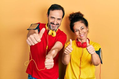 Orta yaşlı bir çift İspanyol kadın ve erkek spor giyer ve kol bandı takar. Elle olumlu jest yapmayı onaylarlar. Başparmakları havada ve başarı için mutludurlar. kazanan jest. 