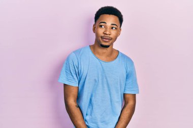 Genç Afro-Amerikan adam, günlük mavi tişört giyiyor. Gülümsüyor, yan tarafa bakıyor ve düşünüyor.. 
