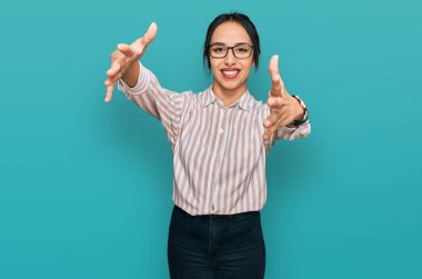 Gündelik kıyafetler ve gözlük takan genç İspanyol kız kameraya sarılıp gülümsüyor. Mutluluğu kucaklayan neşeli bir ifade.. 