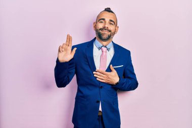 Genç İspanyol bir adam iş elbisesi ve kravat takıyor. Gülümsüyor, yemin ediyor, elleri göğsünde ve parmakları havada küfrediyor. 