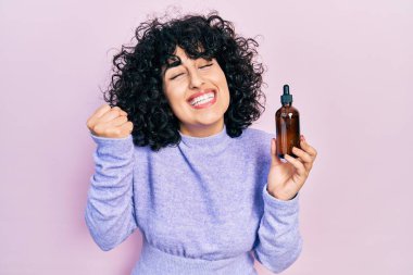 Genç Ortadoğulu kadın gece serumu kullanıyor. Gururla bağırıyor, zaferi kutluyor ve başarıyı kollarını kaldırarak kutluyor. 