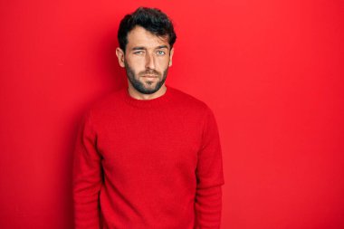 Sakallı, sıradan kırmızı süveter giyen, kuşkucu ve gergin, sorun yüzünden üzgün olan yakışıklı bir adam. negatif kişi. 