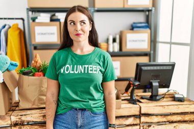 Bağışta gönüllü tişört giyen genç esmer kadın gülümseyip yan tarafa bakıyor ve düşünüyor.. 