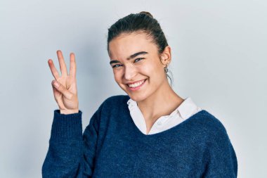 Gündelik kıyafetler giyen genç beyaz kız üç numarayı gösterip işaret ederken kendinden emin ve mutlu bir şekilde gülümsüyor.. 