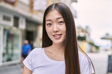 Genç Çinli kız gülümseyerek şehirde mutlu mesut duruyor..