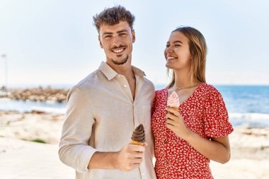 Genç İspanyol çift tatilde gülümseyerek kumsalda dondurma yiyor.