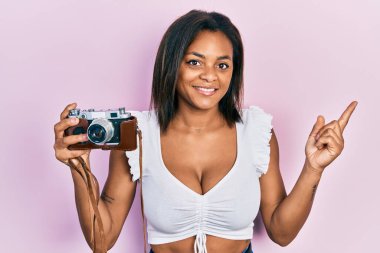 Genç Afro-Amerikalı kız elinde antika kamerayla gülümsüyor mutlu bir şekilde elini ve parmağını yana uzatıyordu. 