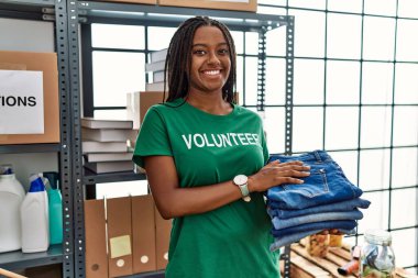 Gönüllü üniforma giyen genç Afrikalı Amerikalı kadın yardım merkezinde katlanmış kot pantolon tutuyor.