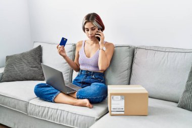 Kafkasyalı genç bir kız laptopla alışveriş yapıyor ve evdeki akıllı telefonla konuşuyor..