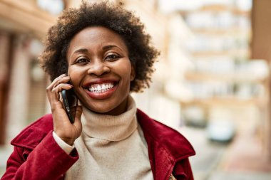 Güzel iş kadını afro saçlı Afro-Amerikan kadın mutlu ve kendinden emin bir şekilde şehirde telefonda konuşuyor.