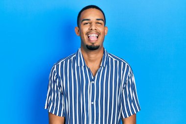 Genç, Afro-Amerikan bir adam günlük kıyafetler giyiyor. Dilini komik bir ifadeyle dışarı çıkarıyor. duygu kavramı. 