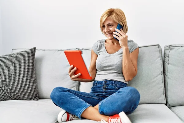 Middle Age Blonde Woman Using Touchpad Talking Smartphone Home — Stockfoto