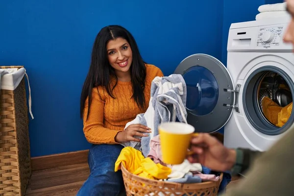 Man and woman couple washing clothes drinking coffee at laundry room