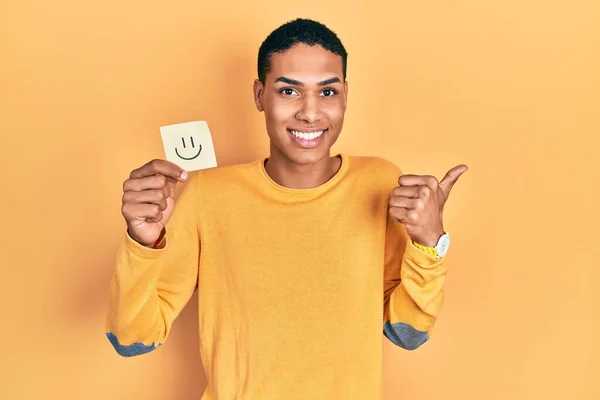 Young African American Guy Holding Smile Reminder Pointing Thumb Side — Foto de Stock