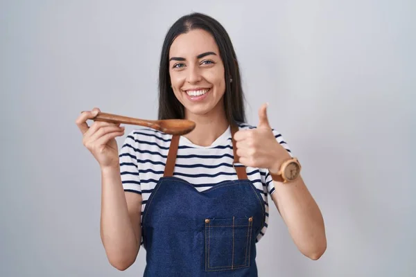 Młoda Brunetka Kobieta Fartuchu Degustacja Żywności Trzymając Drewnianą Łyżkę Uśmiechnięty — Zdjęcie stockowe