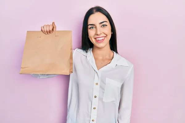 Beautiful woman with blue eyes holding take away paper bag looking positive and happy standing and smiling with a confident smile showing teeth