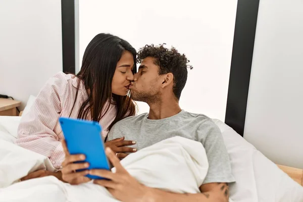 年轻的拉丁男女接吻 用触摸板躺在卧室的床上 — 图库照片