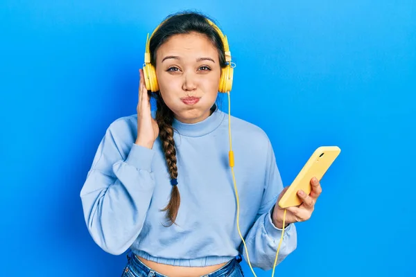 Ung Latinamerikansk Tjej Använder Smartphone Och Hörlurar Puffande Kinder Med — Stockfoto