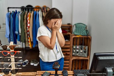 Beautiful middle age hispanic woman working as manager at retail boutique with sad expression covering face with hands while crying. depression concept. 