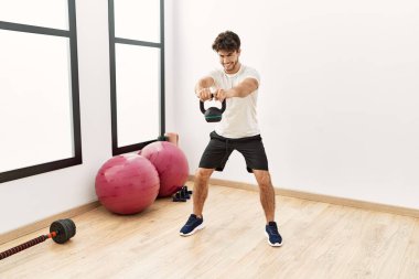 Young hispanic man smiling confident training with kettlebell at sport center