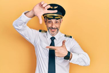 Yakışıklı, orta yaşlı, gri saçlı, uçak pilotu üniforması giyen, gülümseyen, elleri ve parmakları mutlu yüzlü bir adam. yaratıcılık ve fotoğrafçılık kavramı. 