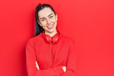 Mavi gözlü, spor kıyafetleri ve kulaklıkları olan mutlu yüzlü, kollarını kavuşturup kameraya bakan güzel bir kadın. pozitif kişi. 