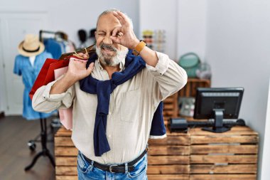Yakışıklı son sınıf öğrencisi butik dükkanında alışveriş torbaları tutuyor. El hareketleriyle gülümsüyor ve mutlu yüzüyle parmaklarının arasından bakıyor.. 