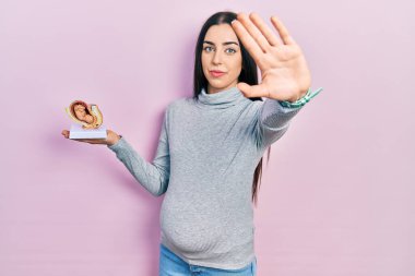Mavi gözlü güzel bir kadın bebek bekliyor. Elinde anatomik bir fetüs var. Eli açık. 