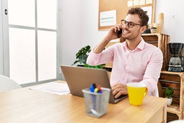 Genç İspanyol gülen adam ofisteki akıllı telefondan konuşuyor.