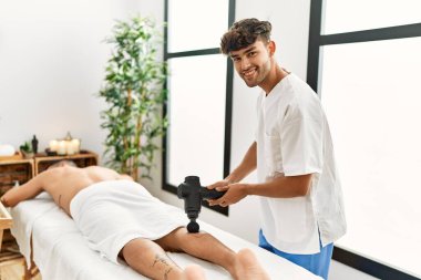 İki İspanyol erkek fizyoterapist ve masaj yapan bacaklar güzellik merkezinde perküsyon tabancası kullanıyorlar.