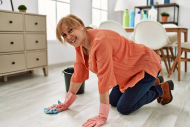 Orta yaşlı kadın gülümsüyor. Evde yerleri temizlerken mutlu..