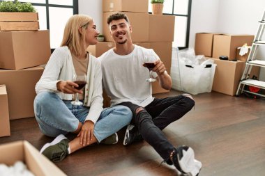 Kırmızı şarap kadehleriyle kadeh kaldıran beyaz bir çift yeni evlerinde oturuyor..