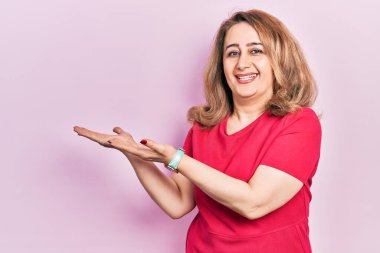 Orta yaşlı beyaz kadın, günlük kıyafetler giyip gülümseyerek içeri girmeye davet ediyor. 