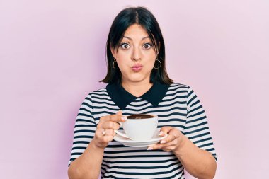 Bir fincan kahve içen genç İspanyol kadın komik yüzlü yanakları şişiriyor. Ağzı havayla şişer, havayı yakalar.. 